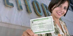 Eleitora segurando o titulo eleitoral na frente da sede do TSE, localizada na Praça dos Tribunais.