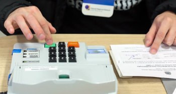 Mesários têm até esta quinta (3) para apresentar justificativa por ausência no 1º turno Imagem de mesário atuando nas Eleições, zoom nas mãos, uma no papel e outra na urna.